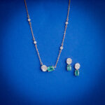 18kt gold diamond pendant set featuring a sleek design with green emerald stones and matching drop earrings.