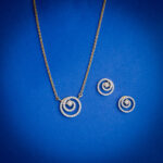 18kt gold diamond pendant set featuring a modern circular swirl design with matching earrings.
