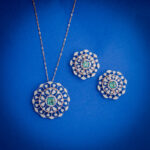 14kt gold diamond pendant set featuring a circular design with emerald centre and matching earrings.
