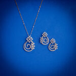 14kt gold diamond pendant set featuring an elegant swirl design with floral diamond clusters and matching earrings.