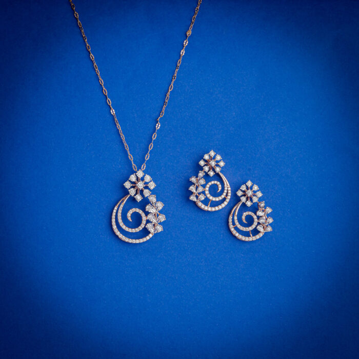 14kt gold diamond pendant set featuring an elegant swirl design with floral diamond clusters and matching earrings.